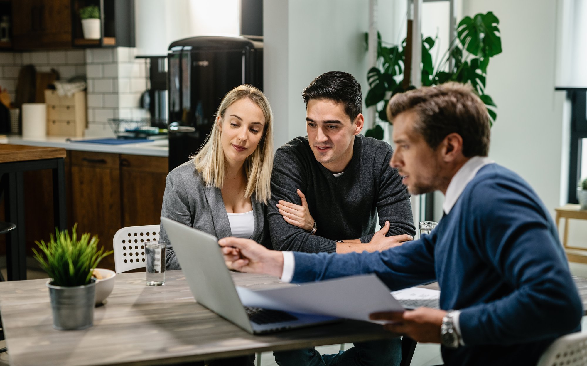 young-couple-real-estate-agent-using-laptop-while-going-through-housing-plan-meeting